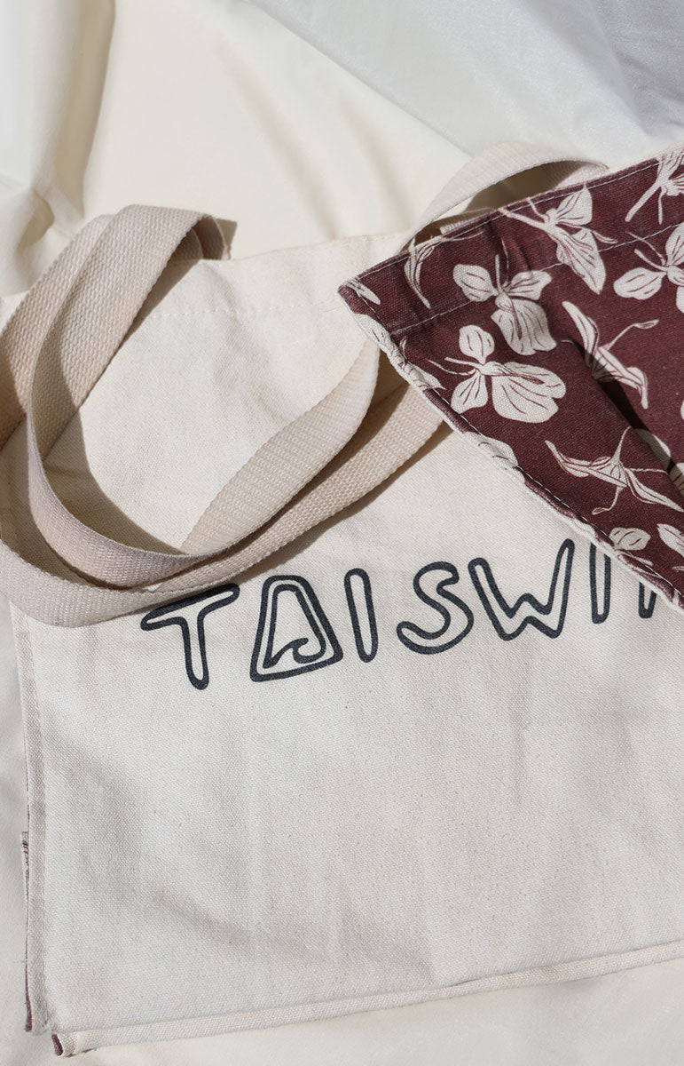 Beige tote bag with 'TAISWIM' branding and a floral-patterned item on top.