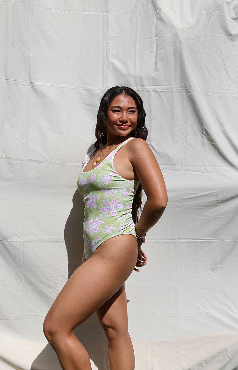 Woman wearing a green and pink floral one-piece swimsuit against a white backdrop tai swim co ella one piece in hawi green and pink light floral trippy pattern from oahu kailua sustainable bikinis hawaiian designed swimsuits