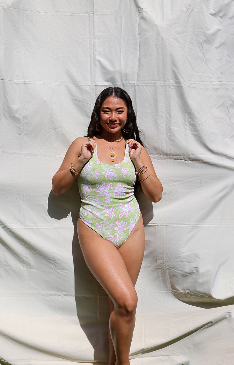 Woman wearing a green and pink floral one-piece swimsuit against a white backdrop tai swim co ella one piece in hawi green and pink light floral trippy pattern from oahu kailua sustainable bikinis hawaiian designed swimsuits