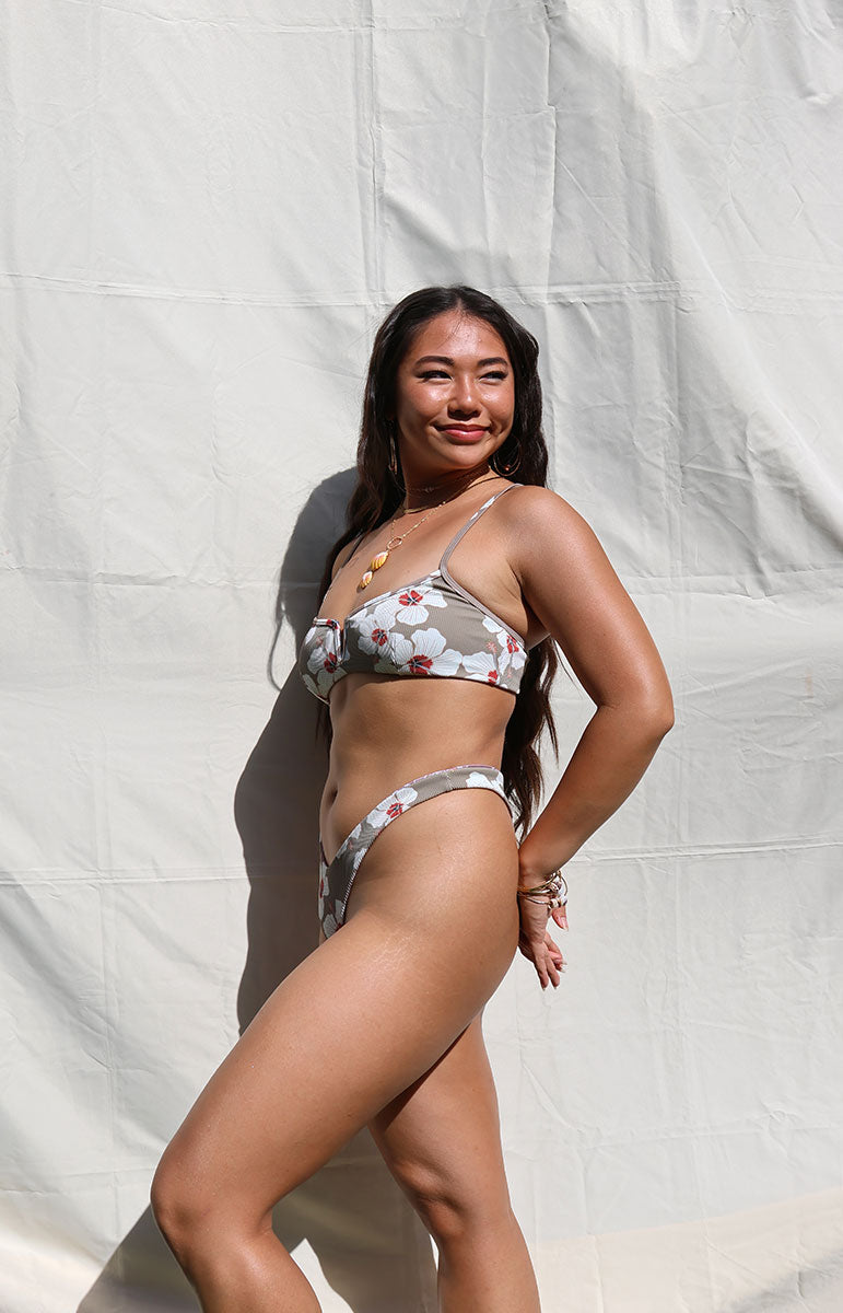 tai swim co haley top in kailua white floral hibiscus print bikini top with v cut scoop neck shape on sunny oahu island hawaii day with sunrise shell necklace in bright lighting with matching mariah bottom in sustainable matching eco friendly fabric skimpy sustainable bikinis from kailua