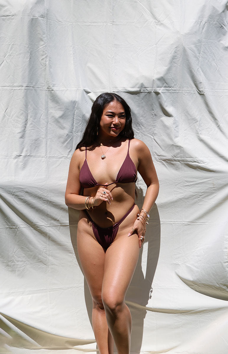 Woman wearing a dark red bikini against a plain white background tai swim co joelle bottom in rose dark maroon ribbed cheeky bikini in all one color reversible cheeky swimwear from hawaii