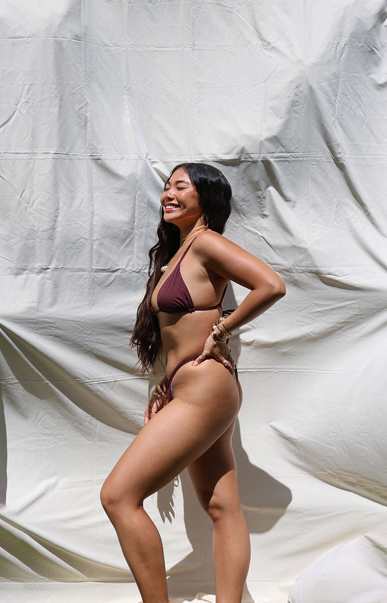 Woman wearing a rose dark maroon brown dark tan bikini against a plain white background rose dark floral earthy triangle bikini top