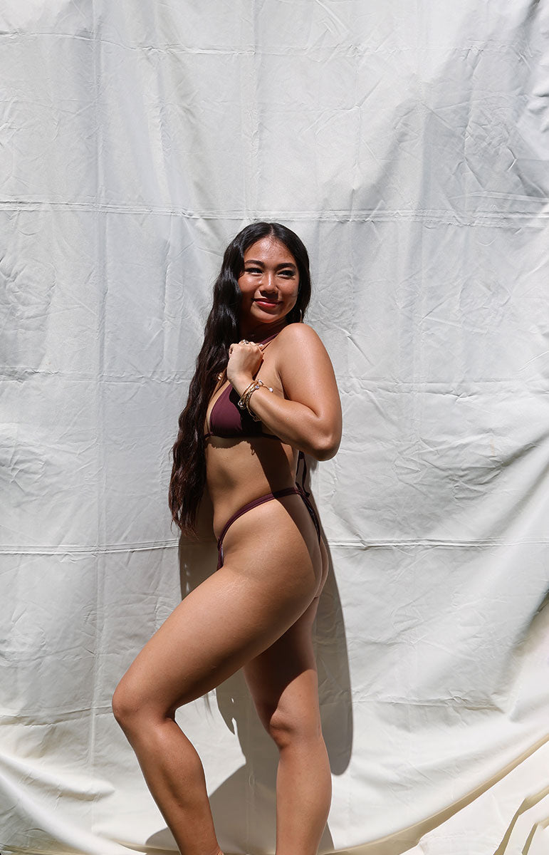 Woman wearing a dark red bikini against a plain white background tai swim co joelle bottom in rose dark maroon ribbed cheeky bikini in all one color reversible cheeky swimwear
