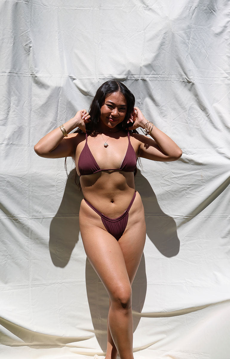 Woman wearing a rose dark maroon brown dark tan bikini against a plain white background rose dark floral earthy triangle bikini top