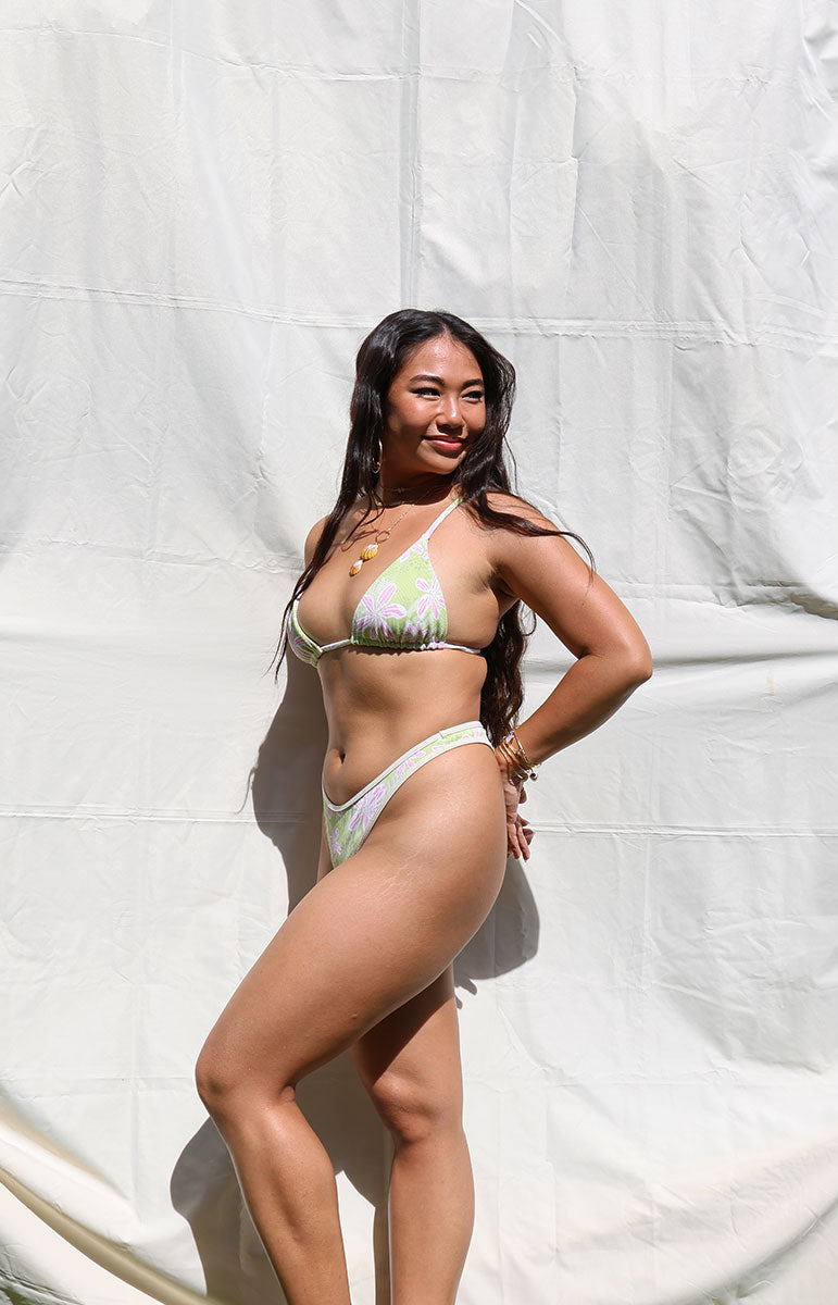 Woman in a bikini standing against a white backdrop Woman wearing a floral bikini against a white background tai swim co joelle top in hawi green and pink floral hibiscus floral vintage hawaii print from kailua oahu hawaii
