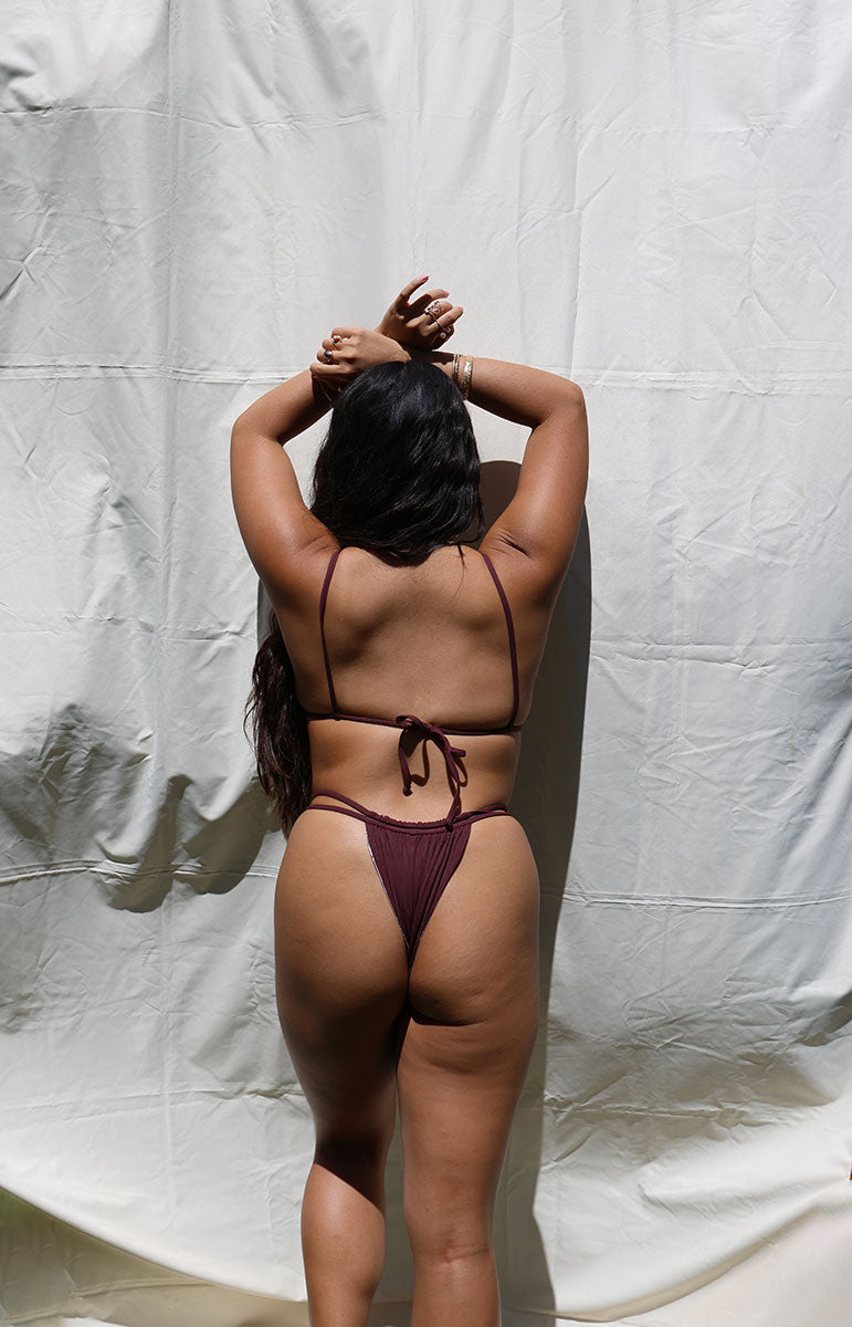 Woman wearing a dark red bikini against a plain white background tai swim co joelle bottom in rose dark maroon ribbed cheeky bikini in all one color reversible cheeky swimwear from hawaii