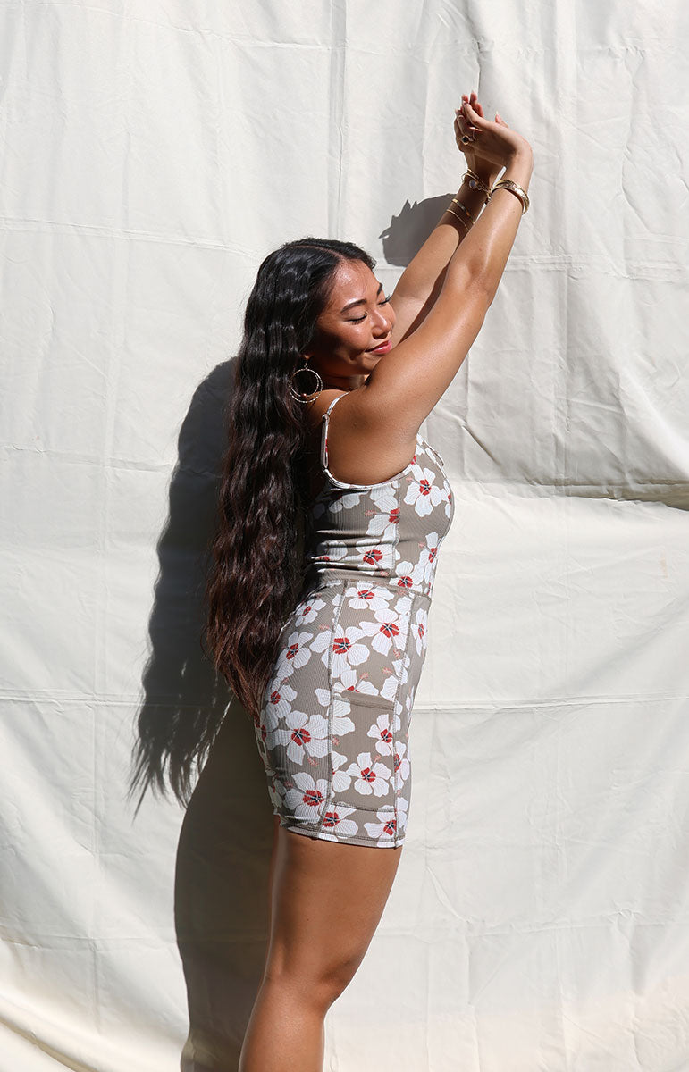 Woman wearing Tai Swim Co's fitted Kimi Romper in ribbed brown Kailua print with white hibiscus flowers, seamless design, photographed from the back in natural light summer 2025 handmade bikini and accessories from the hawaiian islands made from recycled materials
