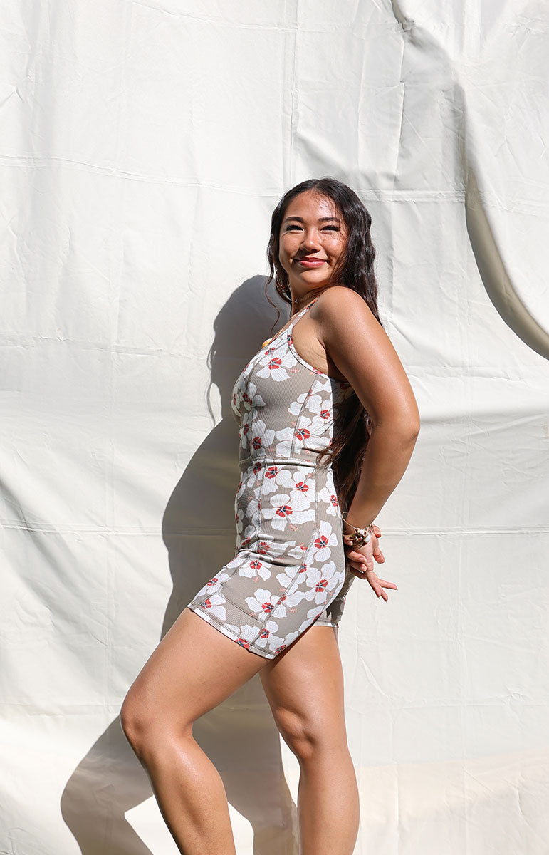 Woman wearing Tai Swim Co's fitted Kimi Romper in ribbed brown Kailua print with white hibiscus flowers, seamless design, photographed from the back in natural light summer 2025 handmade bikini and accessories from the hawaiian islands made from recycled materials tank style flattering fit romper onesie