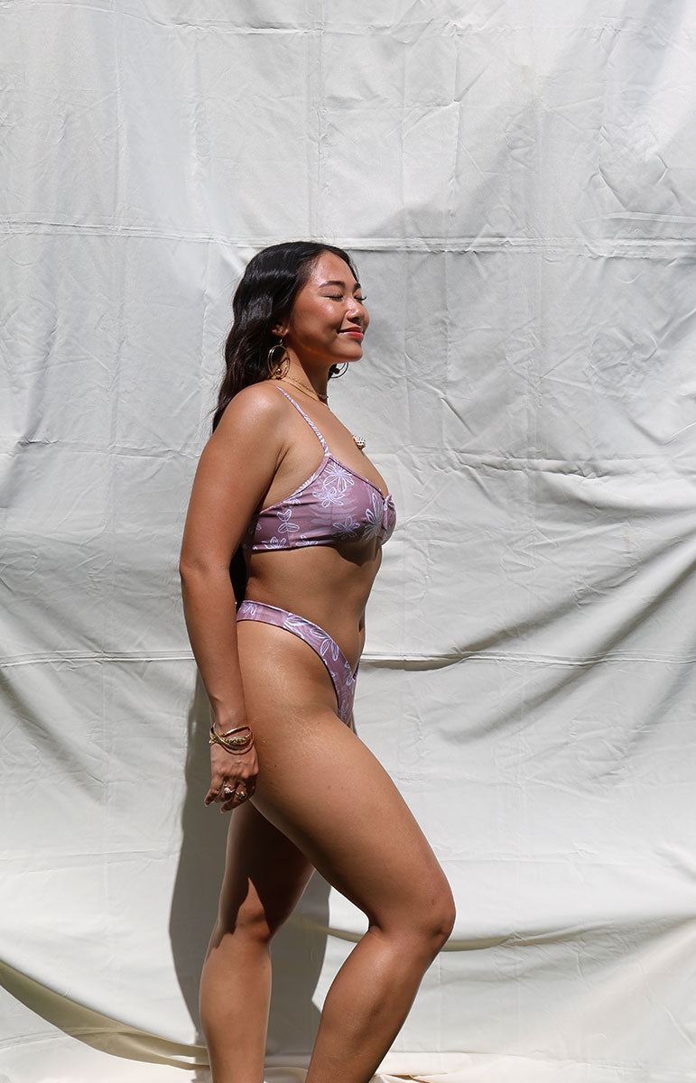 Woman wearing a purple bikini against a plain background Person wearing a purple bikini tai swim kohala lining from oahu with floral patterns against a plain background