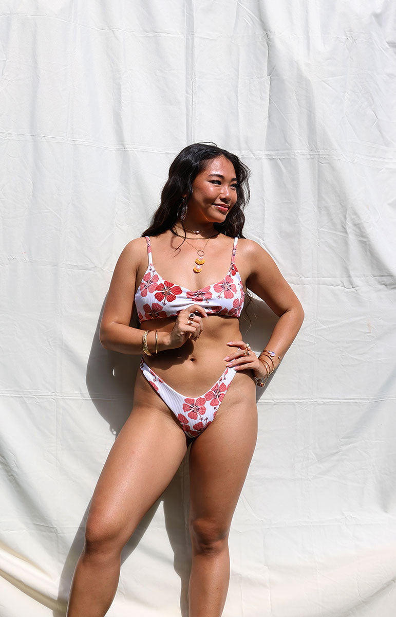 tai swim co cheeky thong bikini bottom in haleiwa red floral hibiscus color print from oahu kailua hawaii minimal coverage bikini set from sustainable hawaiian designer tai swim in kailua on model with dark hair and bralette skimpy top
