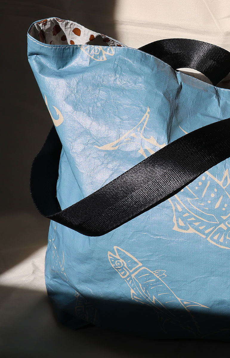 tai swim ahi Blue fish tote bag with black straps and gold hawaiian fish on tyvek bag designs on a dark background