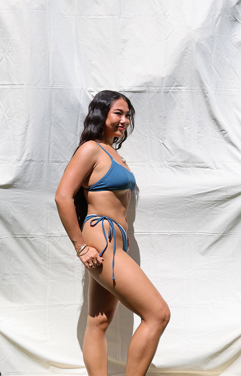 tai swim co rhia bottom in rift dark deep sea blue side tie, adjustable recycled, material swimwear bottom made in Hawaii Kailua Oahu with matching sporty top and bottom, skimpy, minimal coverage, sustainable, material, thin reversible Hawaiian swimwear on model sunny day in hawaii