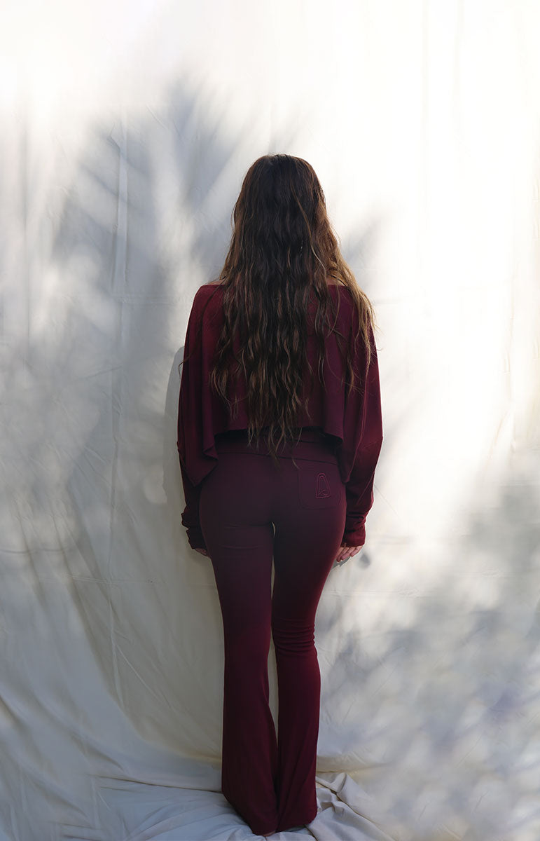 Woman wearing a burgundy outfit standing against a white curtain tai swim co shaiann set in rose comfy cotton lounge ribbed eco friendly cozy sets
