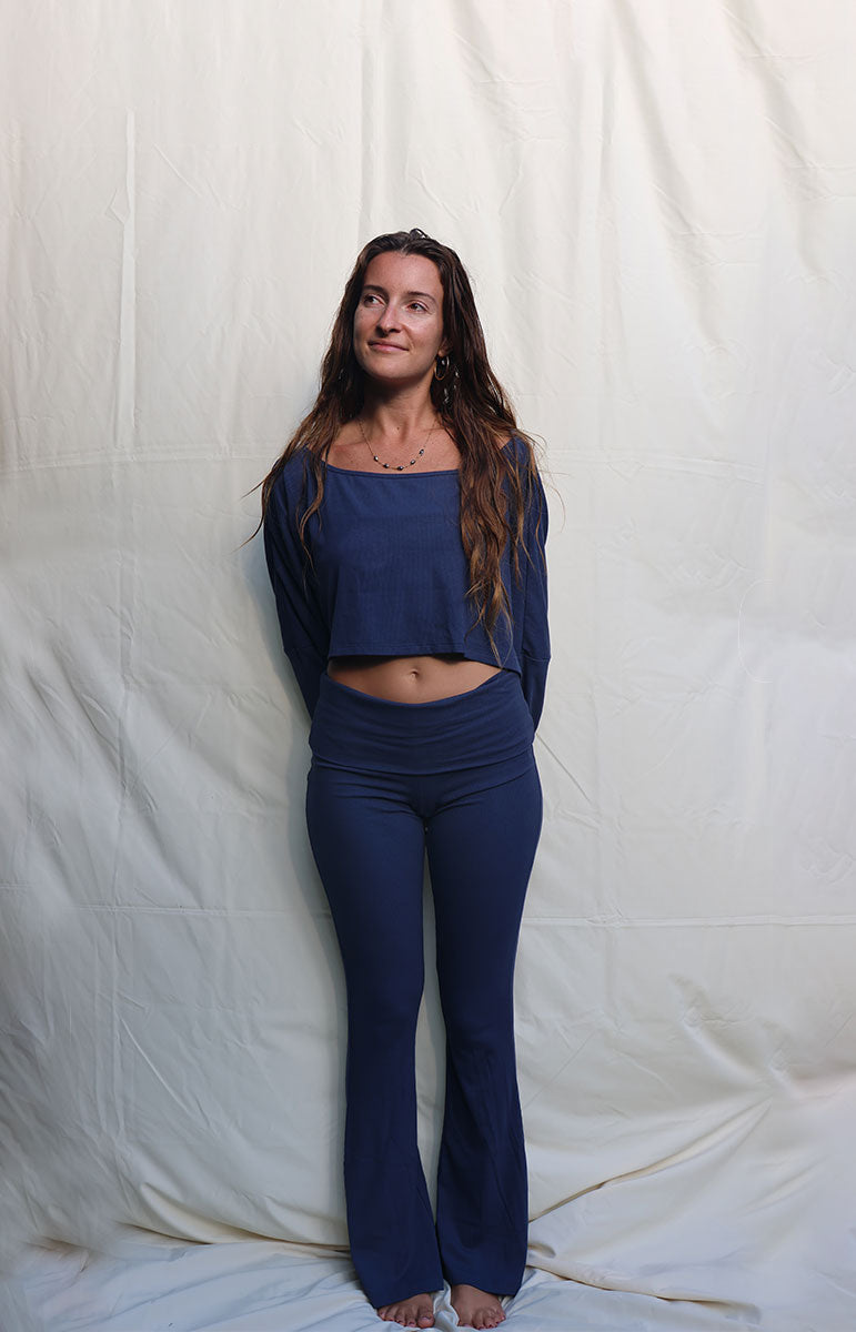 Woman wearing a blue outfit standing against a white backdrop Person wearing a blue outfit standing against a plain white background tai swim co blue navy rift cotton lounge foldover low rise flare pant from hawaii