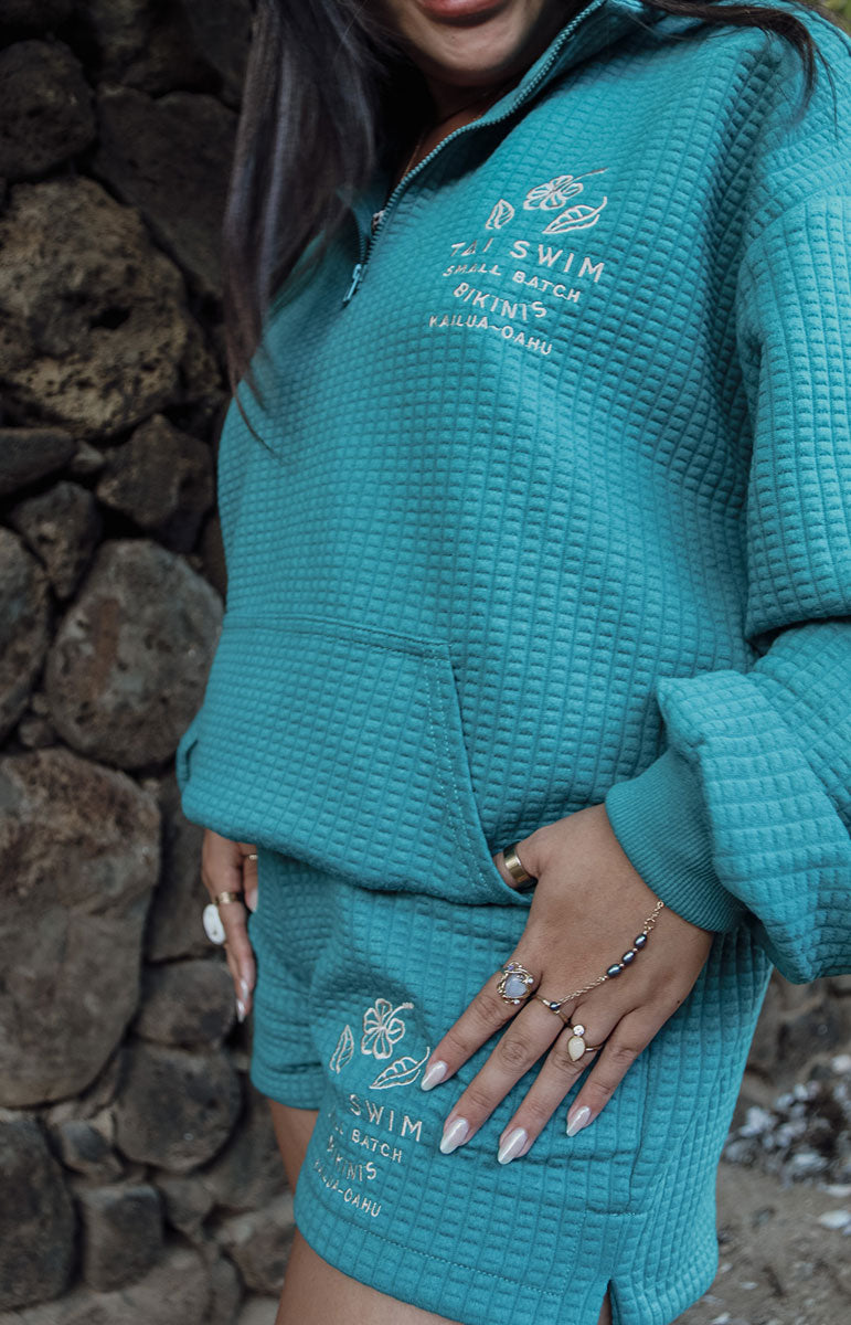 Indulge in Comfort and Style with the Shannah Quarter Zip Sweatshirt by Tai Swim Co. This cozy pullover features a textured design, quarter zip, and puffy sleeves. Made from a recycled waffle cotton/poly blend, it's both chic and sustainable. Available in classic swim colors with a custom Tai Swim logo. Experience ultimate softness and vintage charm in this oversized, relaxed fit. Perfect for post-surf relaxation, this sweatshirt combines a soothing blue tone with tan embroidery for a touch of elegance