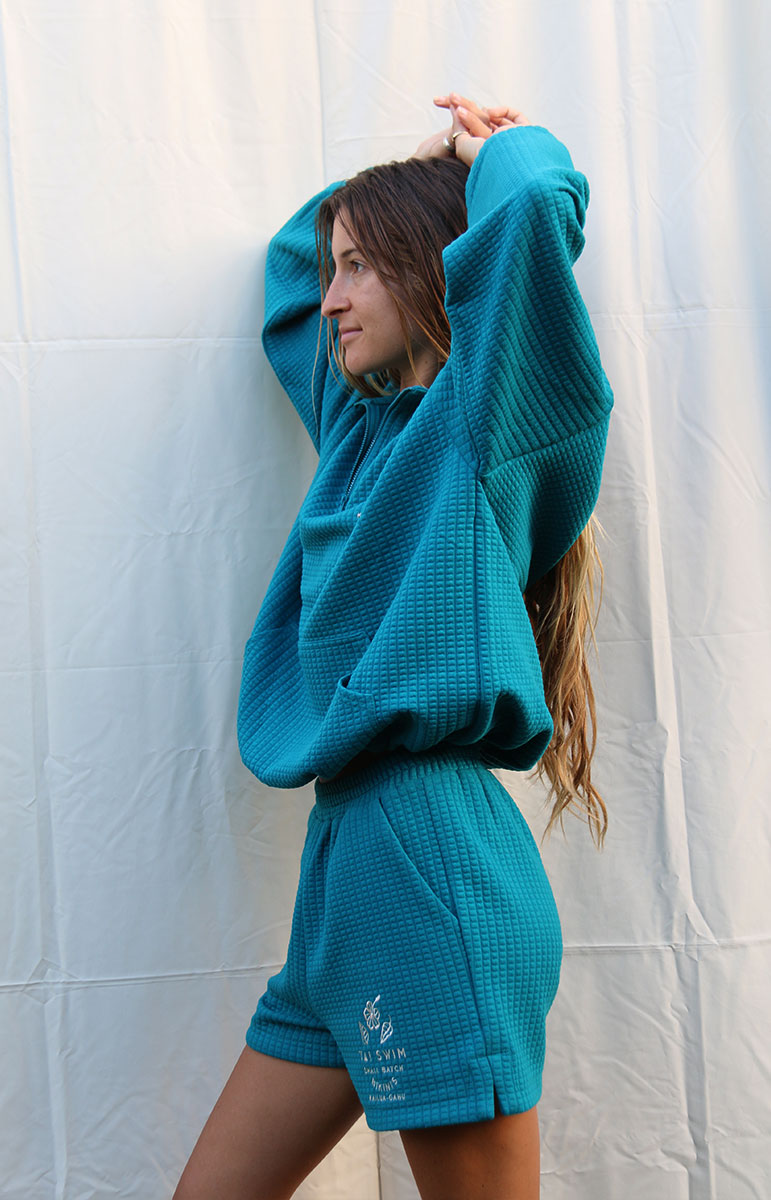 Indulge in Comfort and Style with the Shannah Quarter Zip Sweatshirt by Tai Swim Co. This cozy pullover features a textured design, quarter zip, and puffy sleeves. Made from a recycled waffle cotton/poly blend, it's both chic and sustainable. Available in classic swim colors with a custom Tai Swim logo. Experience ultimate softness and vintage charm in this oversized, relaxed fit. Perfect for post-surf relaxation, this sweatshirt combines a soothing blue tone with tan embroidery for a touch of elegance
