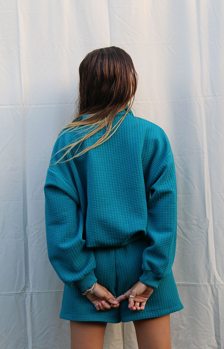 Indulge in Comfort and Style with the Shannah Quarter Zip Sweatshirt by Tai Swim Co. This cozy pullover features a textured design, quarter zip, and puffy sleeves. Made from a recycled waffle cotton/poly blend, it's both chic and sustainable. Available in classic swim colors with a custom Tai Swim logo. Experience ultimate softness and vintage charm in this oversized, relaxed fit. Perfect for post-surf relaxation, this sweatshirt combines a soothing blue tone with tan embroidery for a touch of elegance