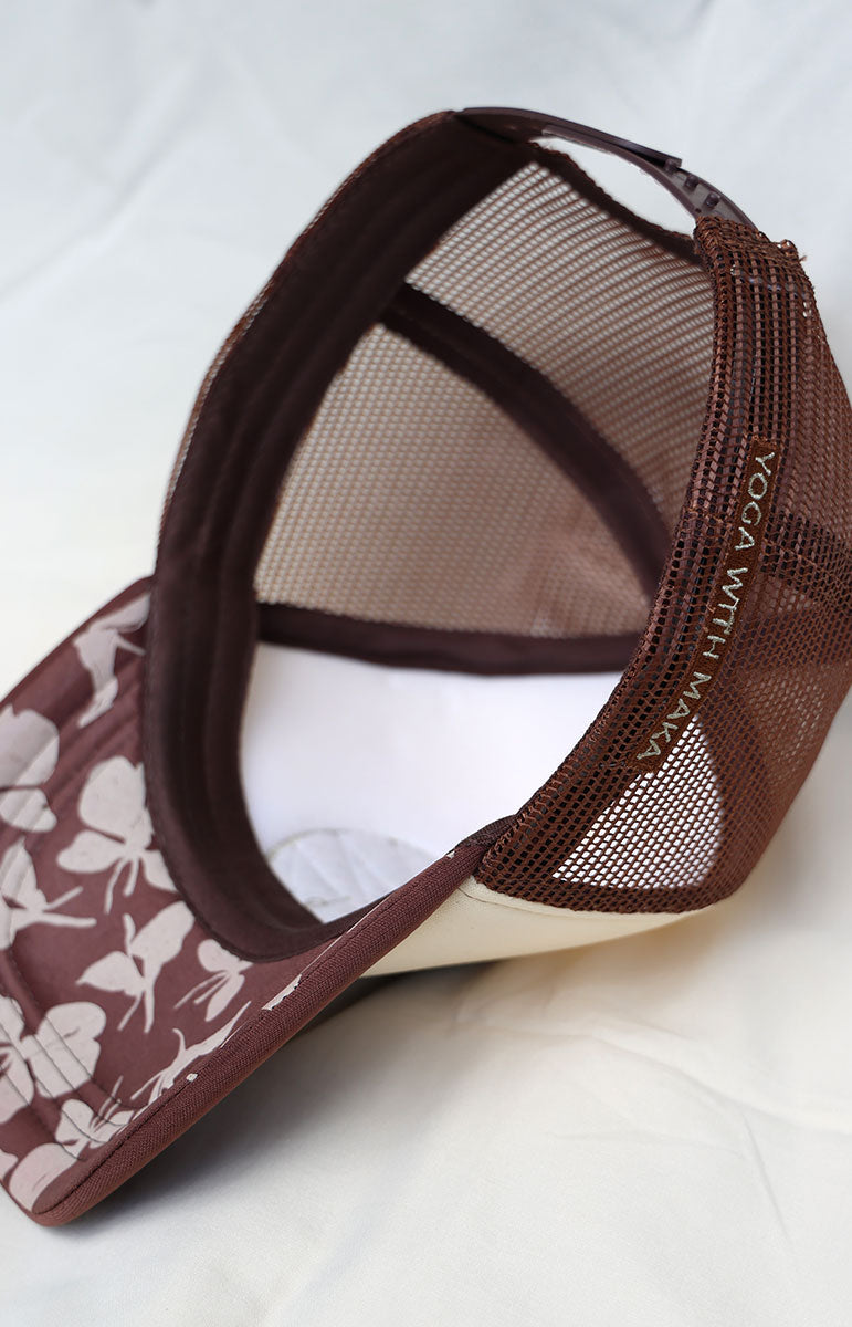 Maroon and beige cap with a tai swim logo in green ginger print on a white background brown yoga with maka collaboration event north shore oahu hawaii floral ginger pattern on the brim