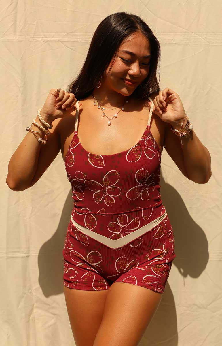 woman wearing tai swim jasmine romper in cowry a red and white shell pattern hawaii jumpsuit for yoga and pockets against a tan background