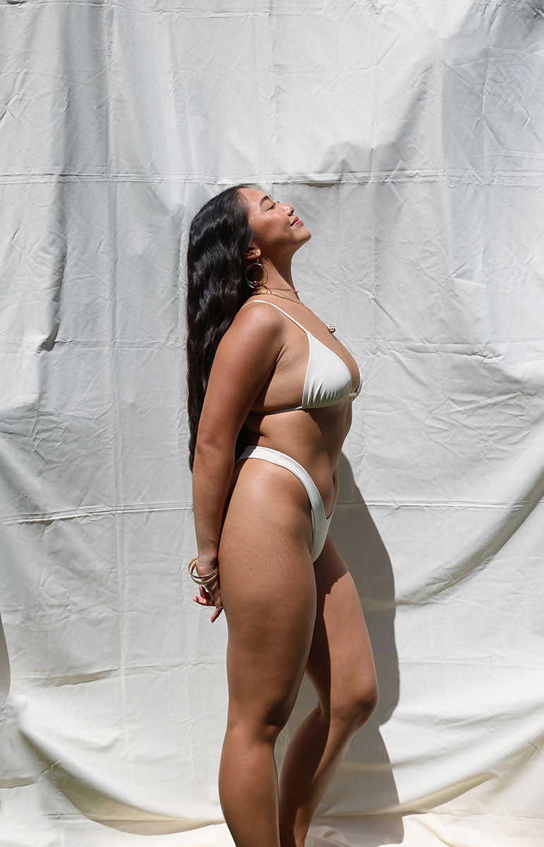 tai swim white haupia coconut joelle top bikini ribbed swimsuit from kailua oahu hawaii reversible cheeky triangle top swimwear on a neutral cloth background with shell jewelry