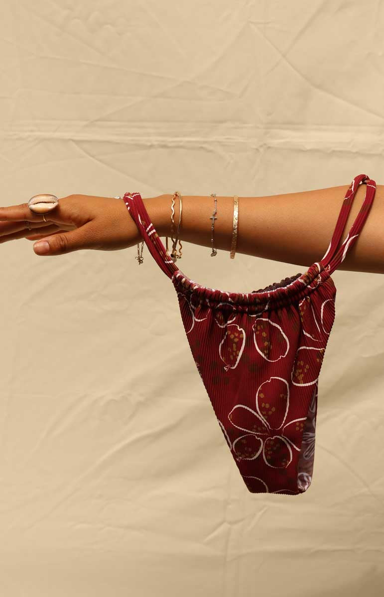 Woman wearing a tai swim cowry joelle bottom double strap stringy red bikini with a cowry shell hawaiian pattern against a beige background
