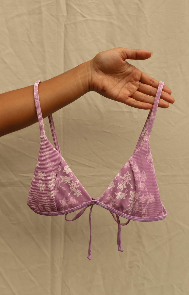 A woman modeling a light purple and white floral print string bikini against a neutral beige backdrop. Tai Swim Manoa print bikini lavender purple swimwear