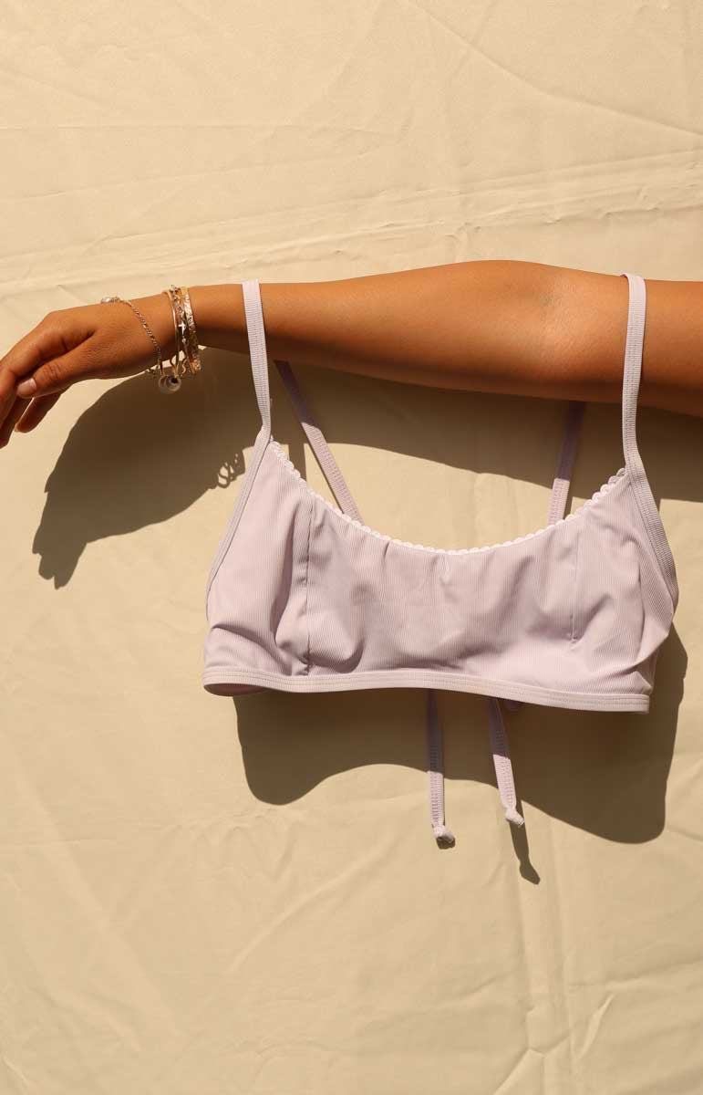 Woman wearing a light purple poni hawaiian bikini against a beige background rhia top and rhia bottom from tai swim co