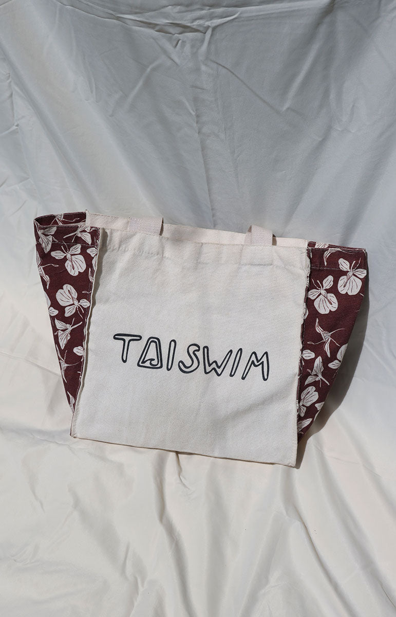 Tote bag with floral design and 'TAISWIM' text on a light gray background