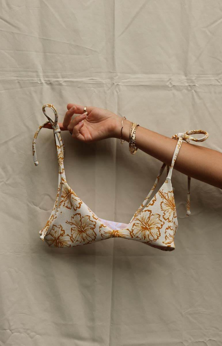 Floral tai swim waimea hawaiian print bikini top held by a hand against a beige background