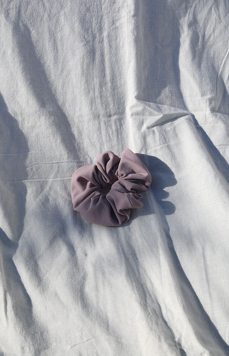 A close-up image of a ribbed swimwear scrunchie in the color UBE, a captivating shade blending tones of purple and pink, reminiscent of the Ube yam. Created using eco-friendly practices in Hawaii, this scrunchie is crafted from upcycled materials, aligning with our commitment to sustainability. The use shade draws its inspiration from the Ube yam, encapsulating the unique blend of purples and pinks found in this nutritious and colorful root vegetable.