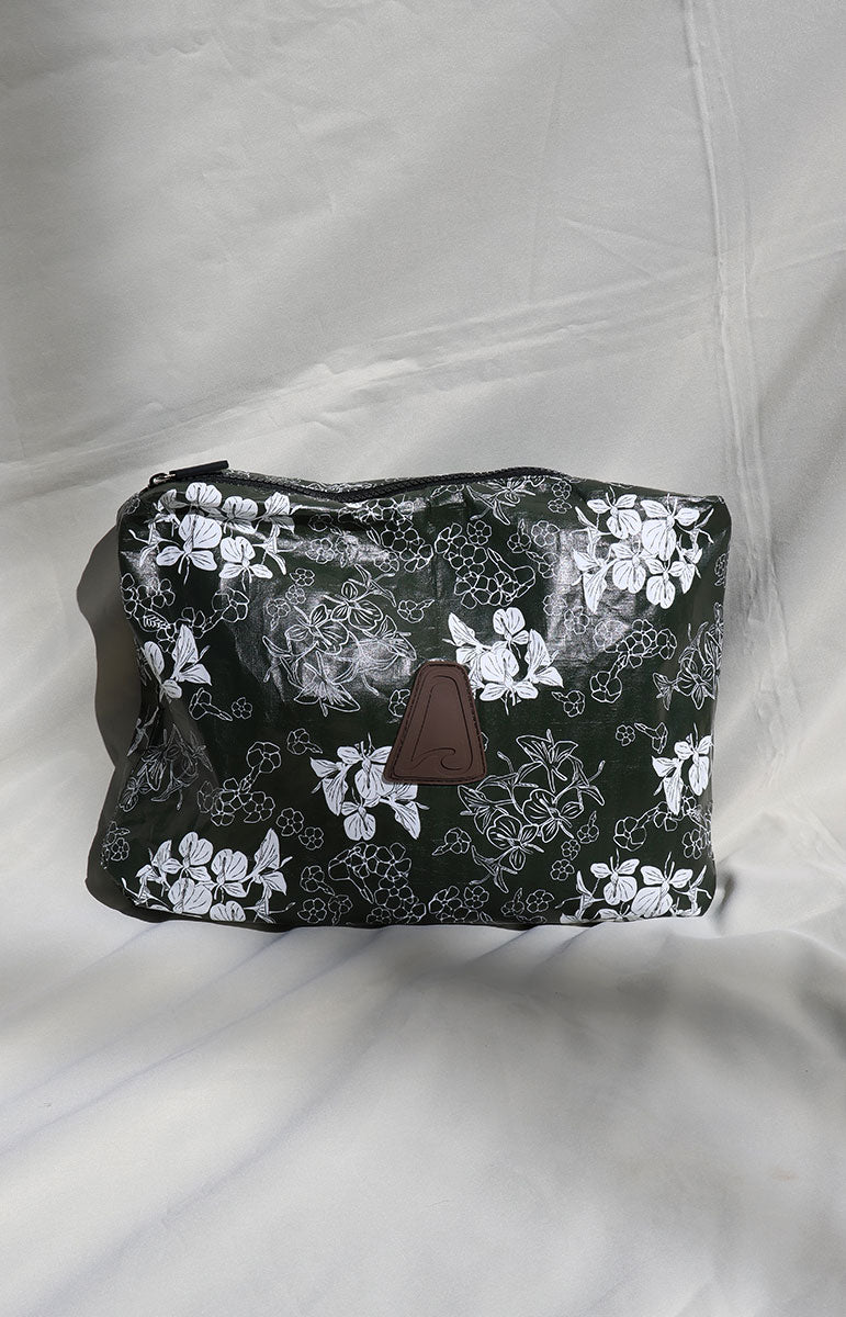 dark green puakenikeni and ginger tai swim co tyvek floral-patterned pouch with a brown patch on a white background