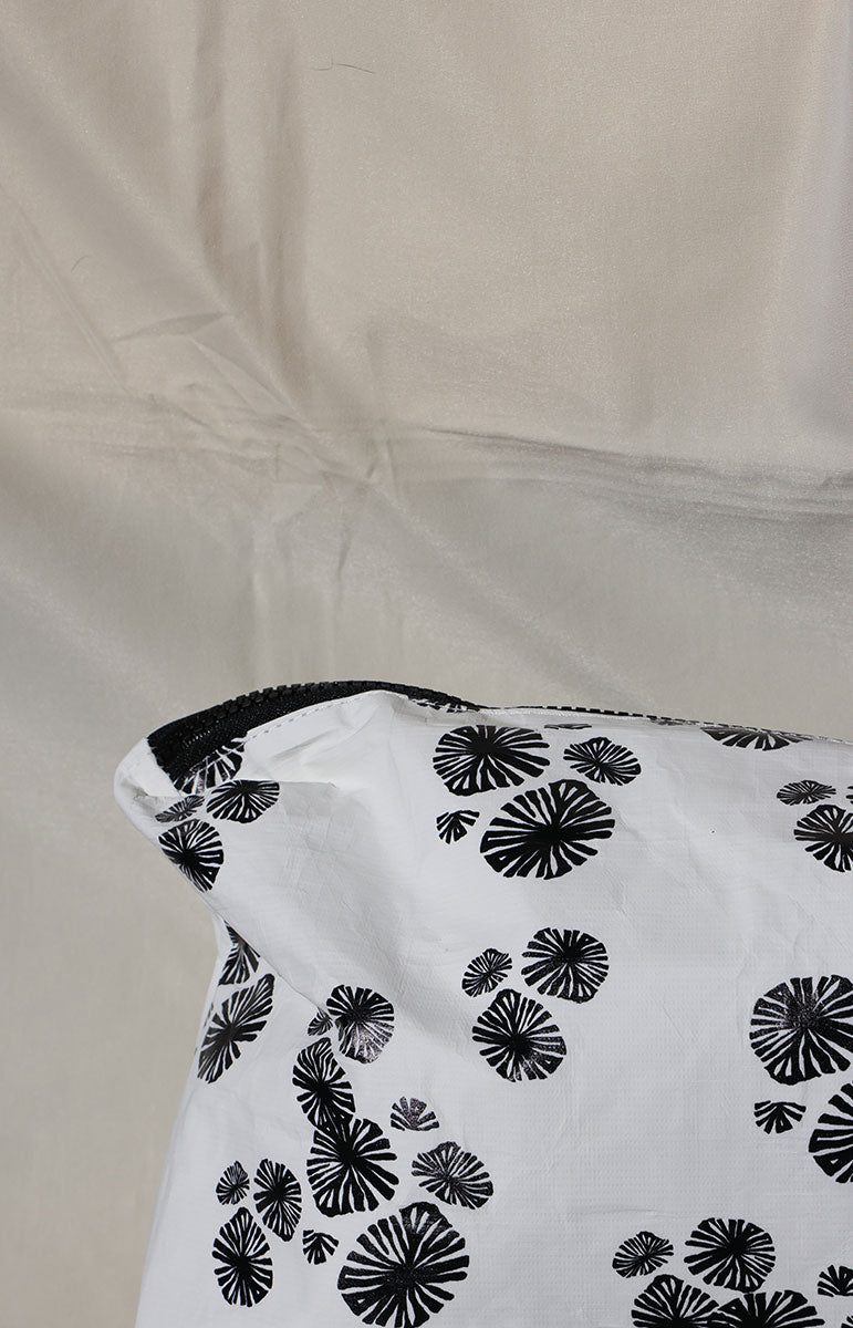 White opihi zipper tyvek bag with black floral patterns on a beige fabric background