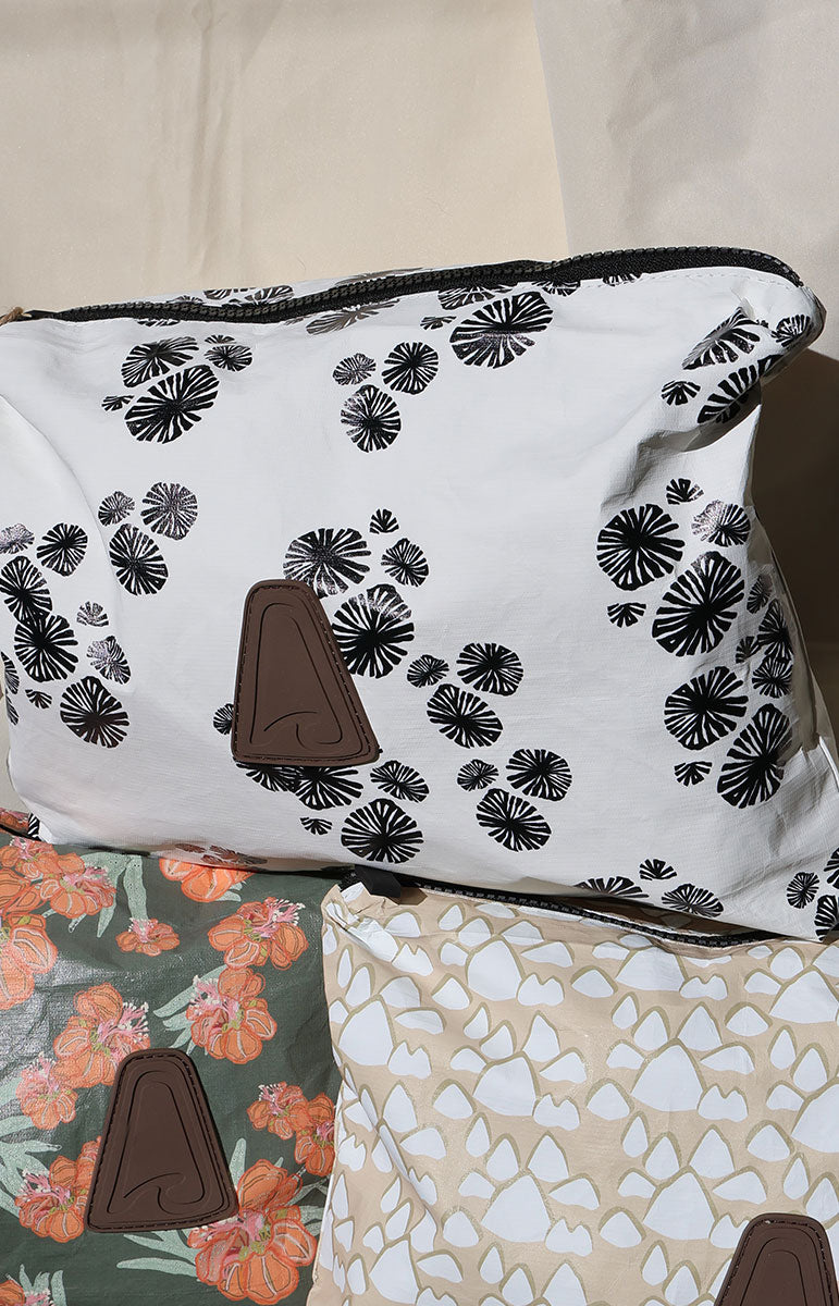 Two tai swim co tyvek recycled pouches with floral waikoloa opihi shell conus shell and geometric hand drawn patterns on a plain background