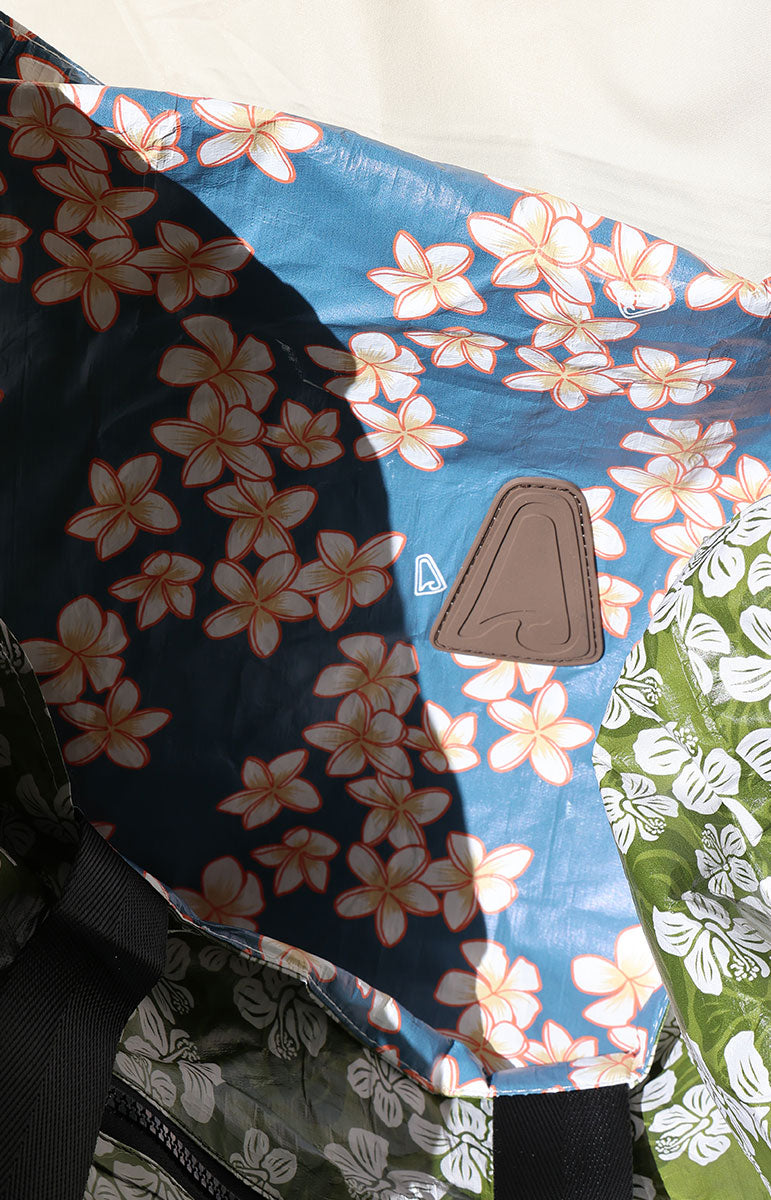 Keiko blue plumeria Floral-patterned tyvek fabric with a blue background and a brown tai swim triangle with wave logo