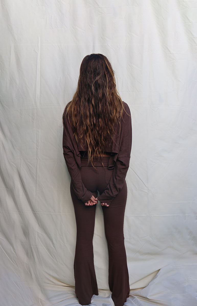 Person wearing a brown outfit standing against a plain white background Woman wearing a brown outfit standing against a white backdrop tai swim co shaiann top long sleeve crop top in espresso
