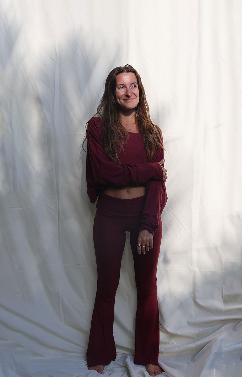 Woman wearing a burgundy outfit standing against a white curtain tai swim co shaiann set in rose comfy cotton lounge ribbed eco friendly cozy sets