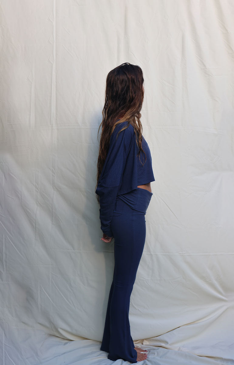 Person wearing a navy blue outfit standing against a plain white background Woman wearing a blue outfit standing against a white background tai swim co shaiann top in rift long sleeve ribbed cotton crop top