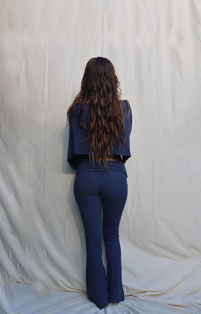 Person wearing a blue outfit standing against a plain white background tai swim co blue navy rift cotton lounge foldover low rise flare pant from hawaii