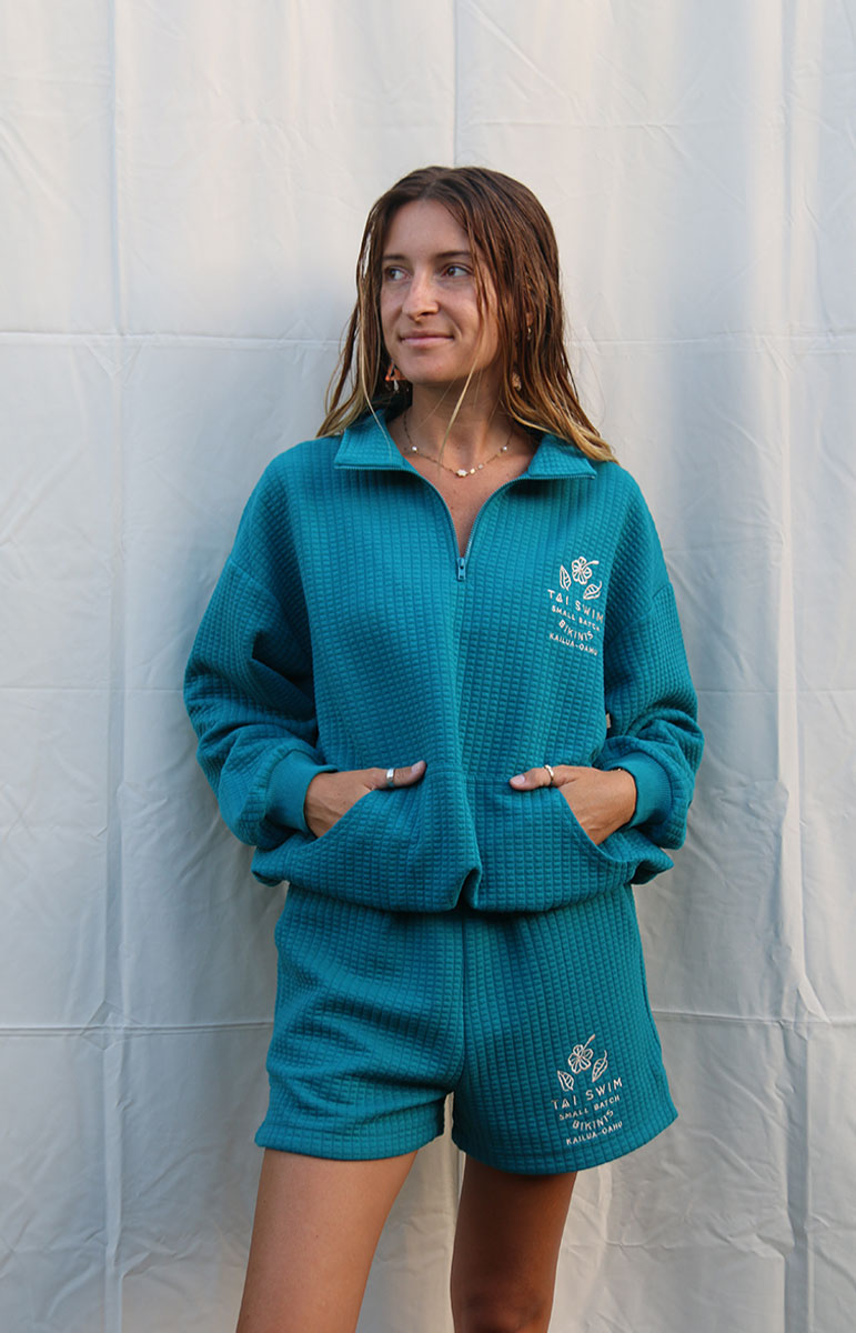 Indulge in Comfort and Style with the Shannah Quarter Zip Sweatshirt by Tai Swim Co. This cozy pullover features a textured design, quarter zip, and puffy sleeves. Made from a recycled waffle cotton/poly blend, it's both chic and sustainable. Available in classic swim colors with a custom Tai Swim logo. Experience ultimate softness and vintage charm in this oversized, relaxed fit. Perfect for post-surf relaxation, this sweatshirt combines a soothing blue tone with tan embroidery for a touch of elegance