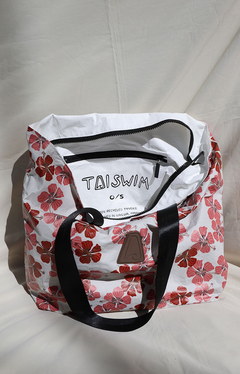 Floral-patterned haleiwa red hibiscus bag with 'TAISWIM' branding on a light background with zippers and brown pvc logo triangle with wave