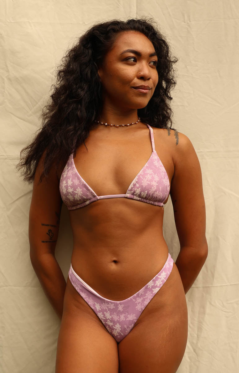 A woman modeling a light pink and white floral print two-piece bikini set against a neutral beige backdrop.