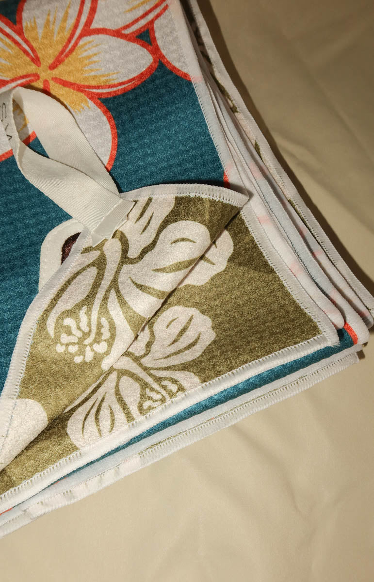 A folded patterned fabric item, likely a towel or blanket, showing a teal blue side with a yellow and orange floral print and a folded side with a brown and white floral pattern.