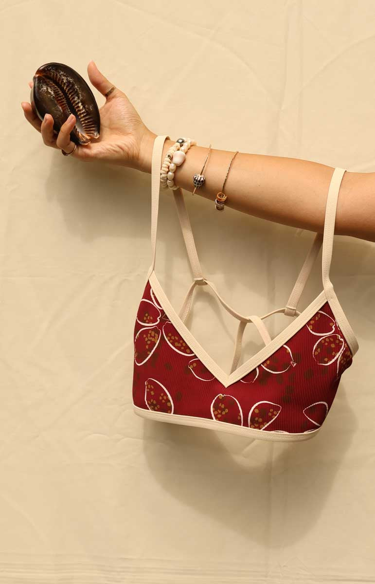 Woman wearing a tai swim maroon cowry shell print red and white bikini against a beige background from hawaii